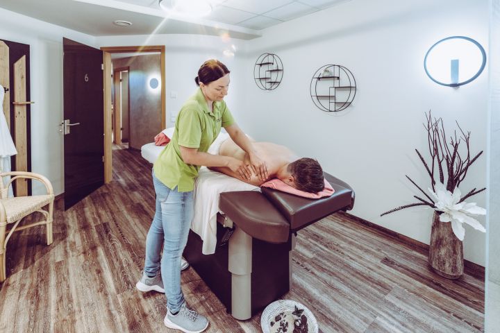 Mann wird auf Liege von Masseurin massiert